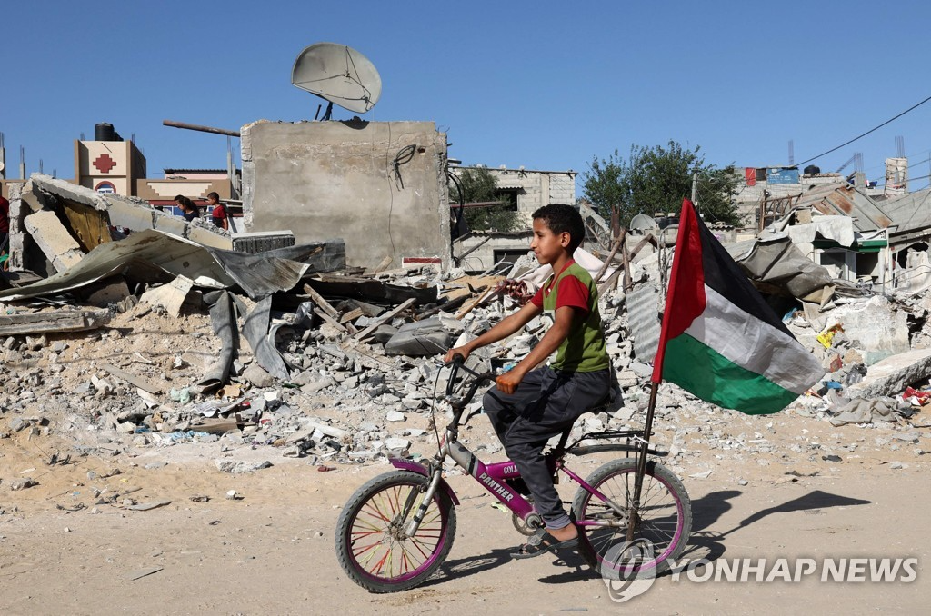 가자지구에서 한 어린이가 자전거에 팔레스타인기를 꽂은 채 공습으로 무너진 건물잔해를 지나고 있다. [AFP=연합뉴스 자료사진]